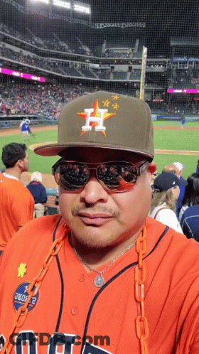 A Man Wearing A Hat With The Letter H On It Stands In Front Of A Baseball Field GIF
