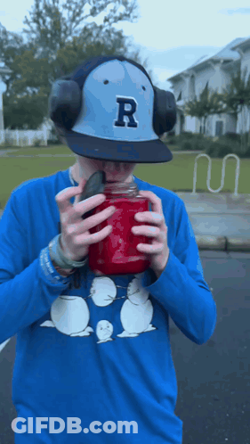 A Man Wearing A Hat With The Letter R On It Is Drinking From A Mason Jar GIF