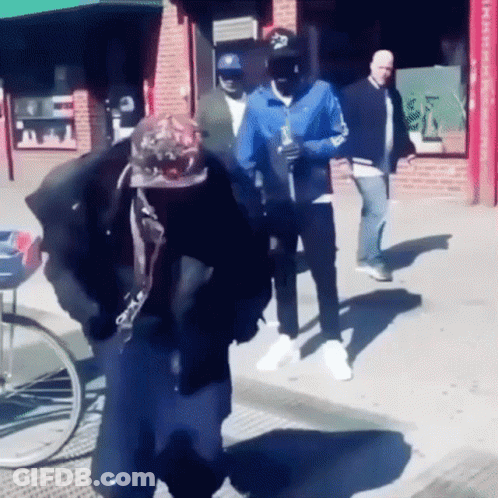 A Man Wearing A Hat With The Letter S On It Walks Down The Street GIF