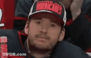 A Man Wearing A Hat With The Word Hurricanes On It Is Sitting In A Stadium . GIF