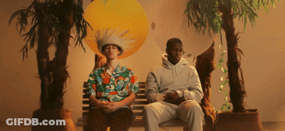 A Man Wearing A Hawaiian Shirt Sits Next To Another Man Wearing A White Hoodie GIF