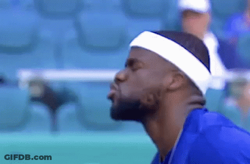 A Man Wearing A Headband And A Blue Shirt Is Blowing A Kiss At The Camera . GIF