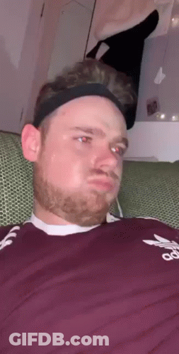 A Man Wearing A Headband And A Maroon Adidas Shirt Is Sitting On A Couch . GIF