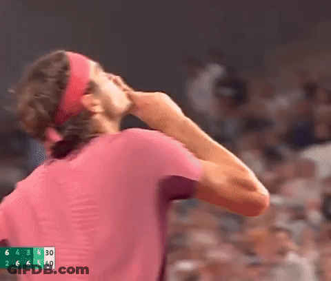 A Man Wearing A Headband And A Pink Shirt Is Standing In Front Of A Crowd And Covering His Face With His Hand . GIF