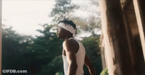 A Man Wearing A Headband And A Tank Top Is Standing In Front Of A Tree . GIF