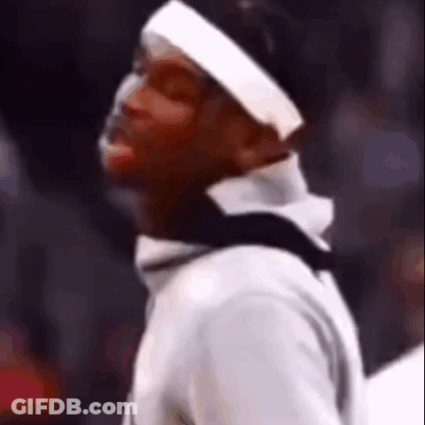 A Man Wearing A Headband And A White Shirt Is Standing In Front Of A Crowd Of People . GIF