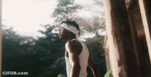 A Man Wearing A Headband And A White Tank Top Is Standing In Front Of A Tree . GIF