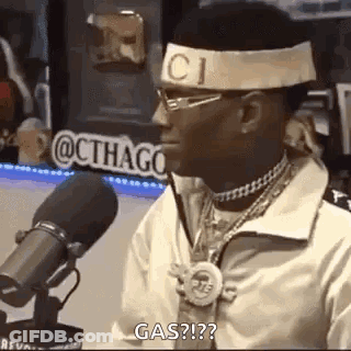 A Man Wearing A Headband And Glasses Is Sitting In Front Of A Microphone And Talking Into It . GIF