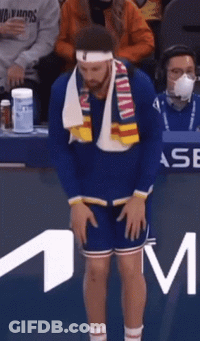 A Man Wearing A Headband And Scarf Is Standing In Front Of A M Logo GIF