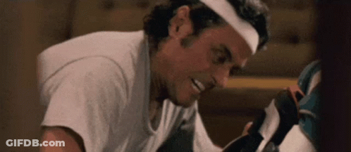 A Man Wearing A Headband Is Smiling While Looking At A Pair Of Shoes . GIF