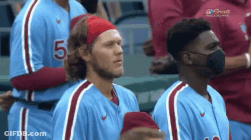 A Man Wearing A Headband With The Number 5 On It Stands Next To A Man Wearing A Mask GIF