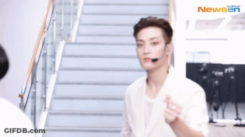 A Man Wearing A Headset Is Walking Down A Set Of Stairs With The Newsen Logo In The Background GIF