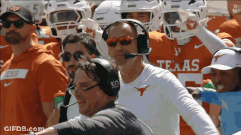 A Man Wearing A Headset Stands In Front Of A Texas Football Team GIF