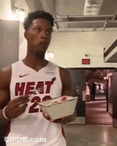 A Man Wearing A Heat Jersey Is Holding A Box Of Food GIF
