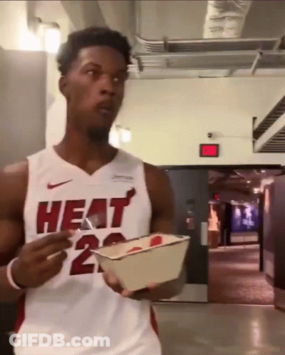 A Man Wearing A Heat Jersey Is Holding A Container Of Food GIF