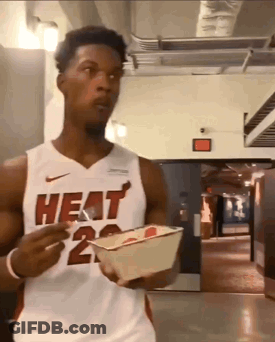 A Man Wearing A Heat Jersey Is Holding A Container Of Food GIF