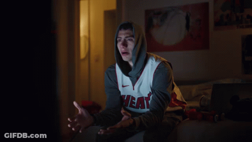 A Man Wearing A Heat Jersey Sits On A Bed At Night GIF