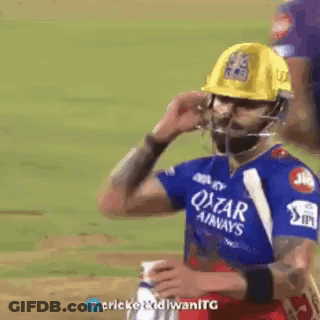A Man Wearing A Helmet And A Blue Shirt Is Standing On A Cricket Field . GIF