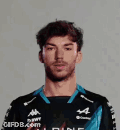 A Man Wearing A Helmet And A Castrol Shirt Is Standing In Front Of A White Wall . GIF