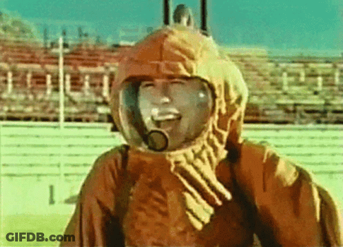 A Man Wearing A Helmet And A Hood Is Smiling In Front Of A Stadium GIF