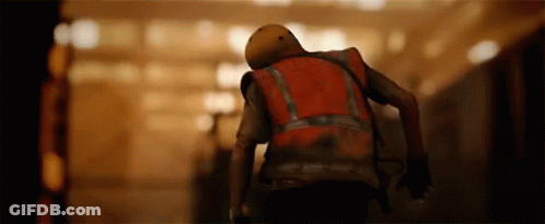A Man Wearing A Helmet And A Red Vest Is Walking Down A Hallway . GIF
