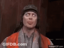 A Man Wearing A Helmet And An Orange Vest Is Making A Face . GIF