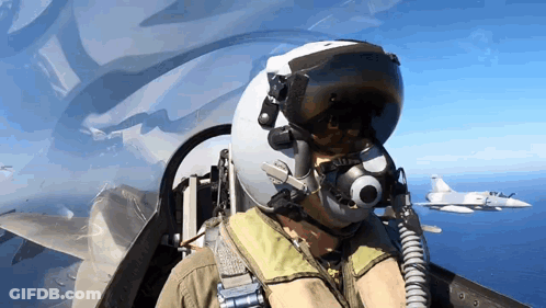 A Man Wearing A Helmet And Goggles Is Flying A Fighter Jet Over The Ocean GIF