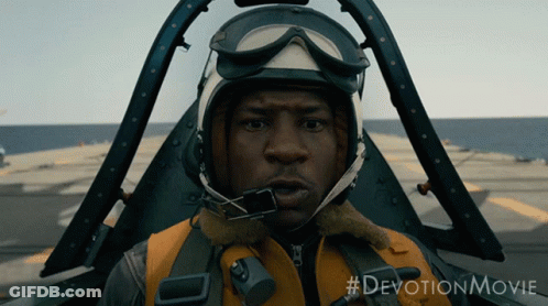 A Man Wearing A Helmet And Goggles Is Sitting In A Plane With The #Devotionmovie Written Below Him GIF