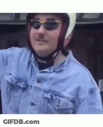 A Man Wearing A Helmet And Sunglasses Is Standing In A Car . GIF