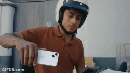 A Man Wearing A Helmet Holds A White Iphone GIF