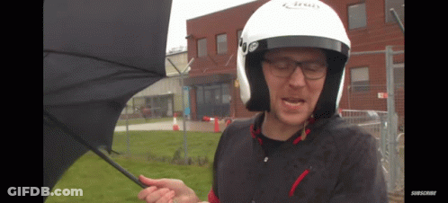 A Man Wearing A Helmet Is Holding An Umbrella In Front Of A Building GIF