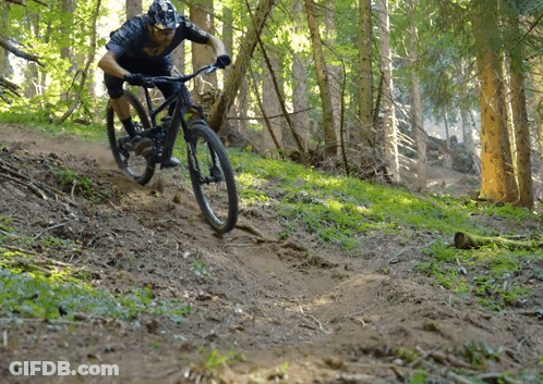 A Man Wearing A Helmet Is Riding A Bike Down A Trail In The Woods GIF