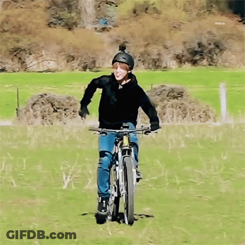 A Man Wearing A Helmet Is Riding A Bike On A Grassy Field GIF