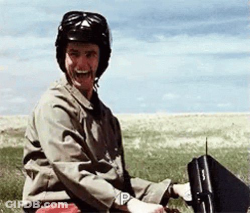 A Man Wearing A Helmet Is Sitting In A Field Holding A Briefcase With The Letter P On It GIF