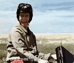 A Man Wearing A Helmet Is Sitting In A Field With A Briefcase And A Gun . GIF