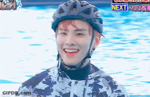 A Man Wearing A Helmet Is Smiling In Front Of A Sign That Says Next . GIF