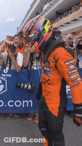 A Man Wearing A Helmet Is Standing In Front Of A Crowd Of People At A Race Track . GIF