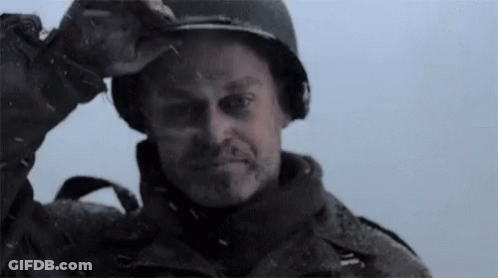 A Man Wearing A Helmet Is Standing In The Snow And Looking At The Camera . GIF