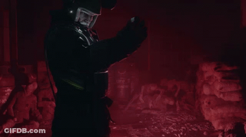 A Man Wearing A Helmet Stands In A Dark Room With Barrels That Say ' Top ' On Them GIF
