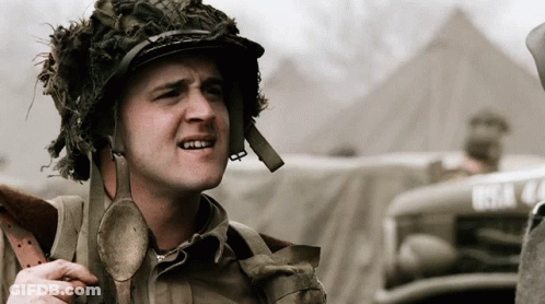 A Man Wearing A Helmet With A Spoon Around His Neck Is Standing In Front Of A Vehicle With The License Plate Bsa 44 GIF