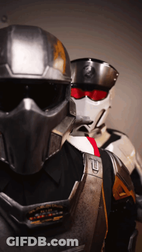 A Man Wearing A Helmet With The Letter T On It Is Standing Next To Another Man GIF