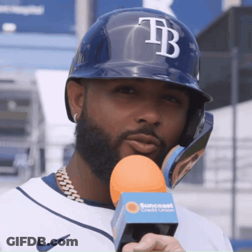 A Man Wearing A Helmet With The Letter Tb On It Holds An Orange Microphone GIF