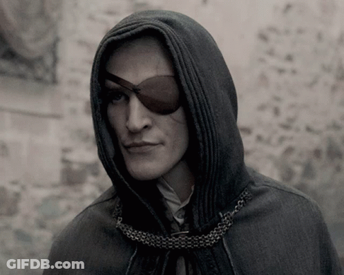 A Man Wearing A Hooded Cape And An Eye Patch Looks At The Camera GIF