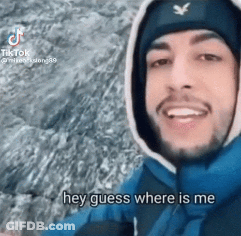A Man Wearing A Hooded Jacket And A Beanie Is Smiling And Says Hey Guess Where Is Me GIF