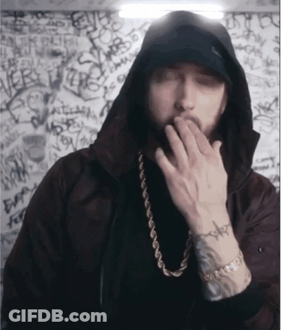 A Man Wearing A Hooded Jacket And A Gold Chain Covering His Mouth GIF