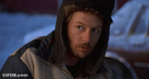 A Man Wearing A Hooded Jacket And Ear Warmers Looks At The Camera GIF