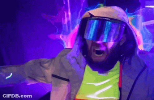 A Man Wearing A Hooded Jacket And Goggles Is Standing In Front Of A Purple Background GIF