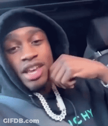 A Man Wearing A Hooded Sweatshirt And A Chain Around His Neck Is Sitting In A Car . GIF
