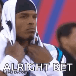 A Man Wearing A Hooded Sweatshirt And A Headband Is Sitting In A Crowd Of People . GIF