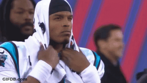 A Man Wearing A Hooded Sweatshirt And A Headband Is Standing In Front Of A Crowd . GIF
